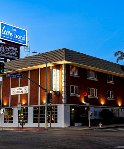 A street view of a brick hotel with bright signage and palm trees under a clear blue sky.