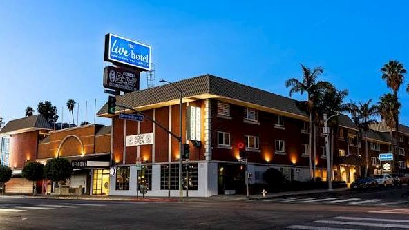 A roadside view of the Live Hotel building at dusk with palm trees and a bright blue sky.